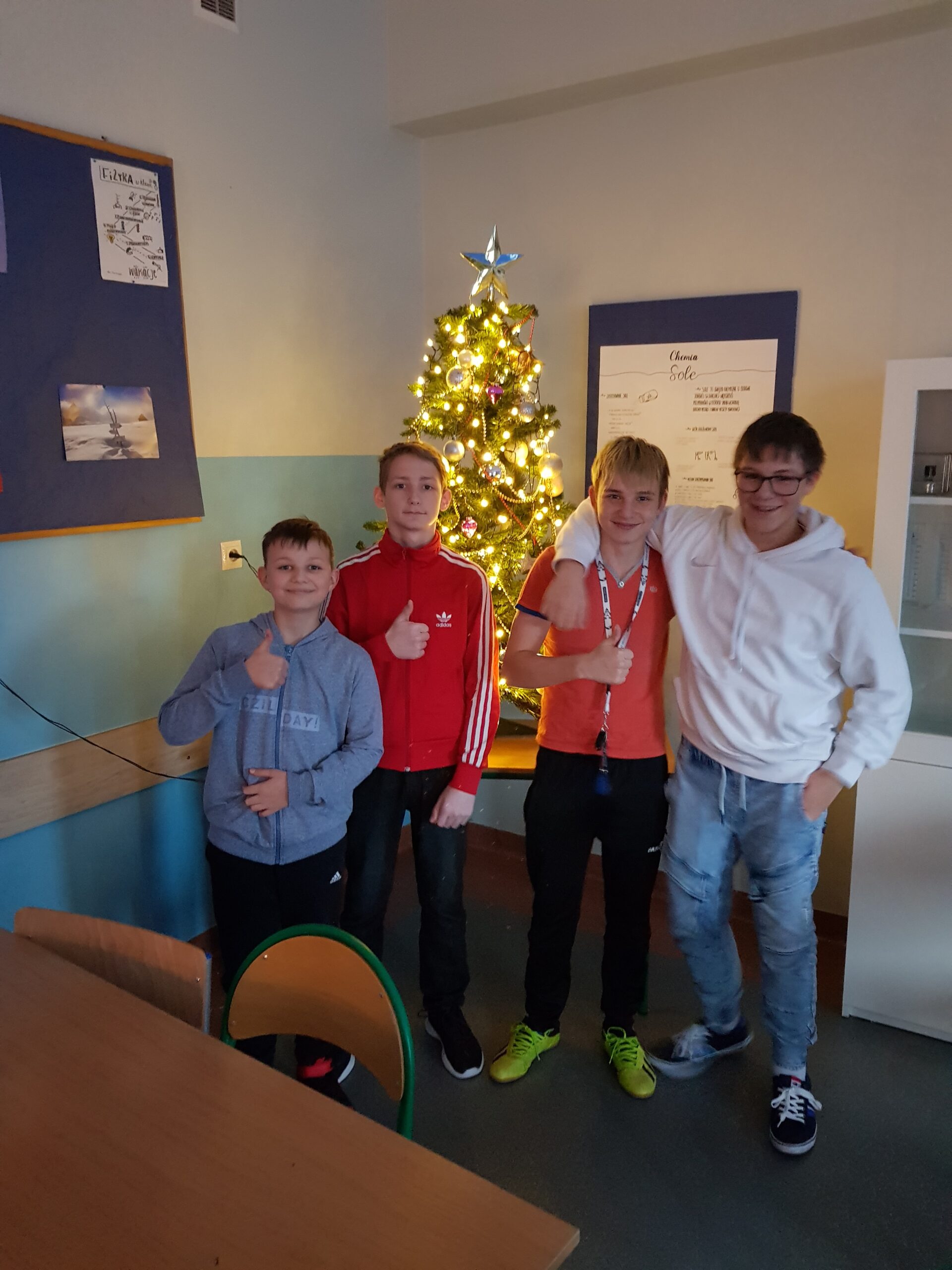 Zdjęcie przedstawia uczniów klasy 7a w sali lekcyjnej. W tle świąteczna choinka.