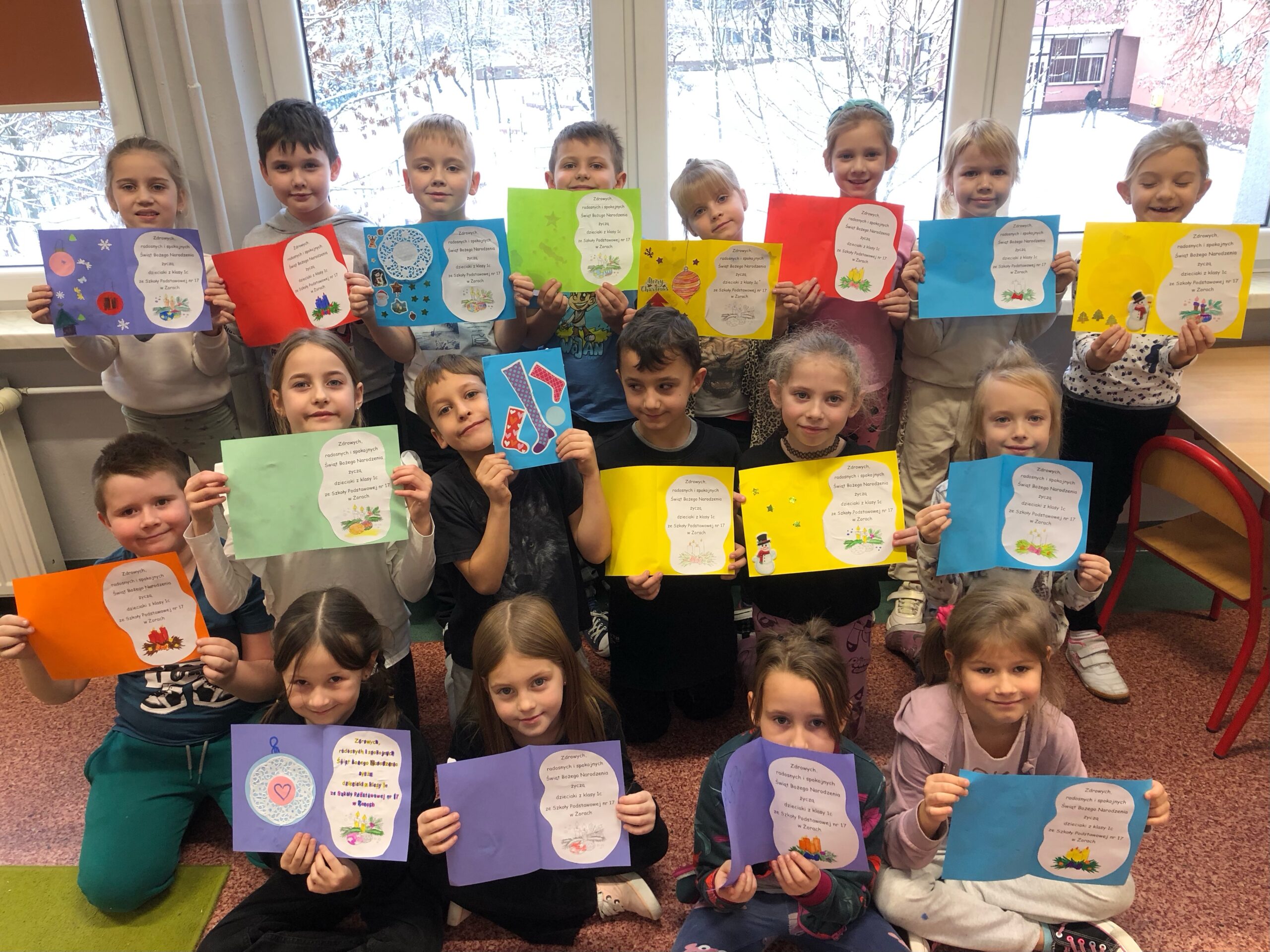Zdjęcie przedstawia uczniów klasy 1c, którzy trzymają w rękach kartki świąteczne wykonane dla podopiecznych Domu Pomocy Społecznej w Żorach.